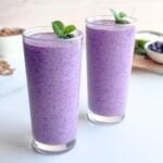 Two glasses of blueberry bran smoothie garnished with fresh mint leaves.