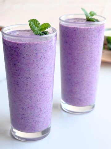 Two glasses of blueberry bran smoothie garnished with fresh mint leaves.