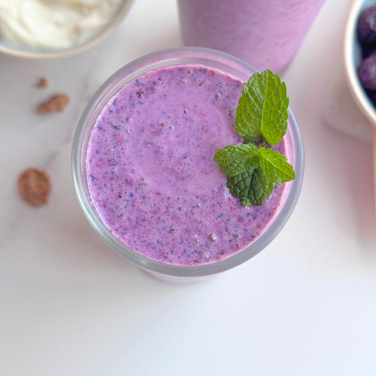 Overhead view of a creamy blueberry bran smoothie garnished with fresh mint.