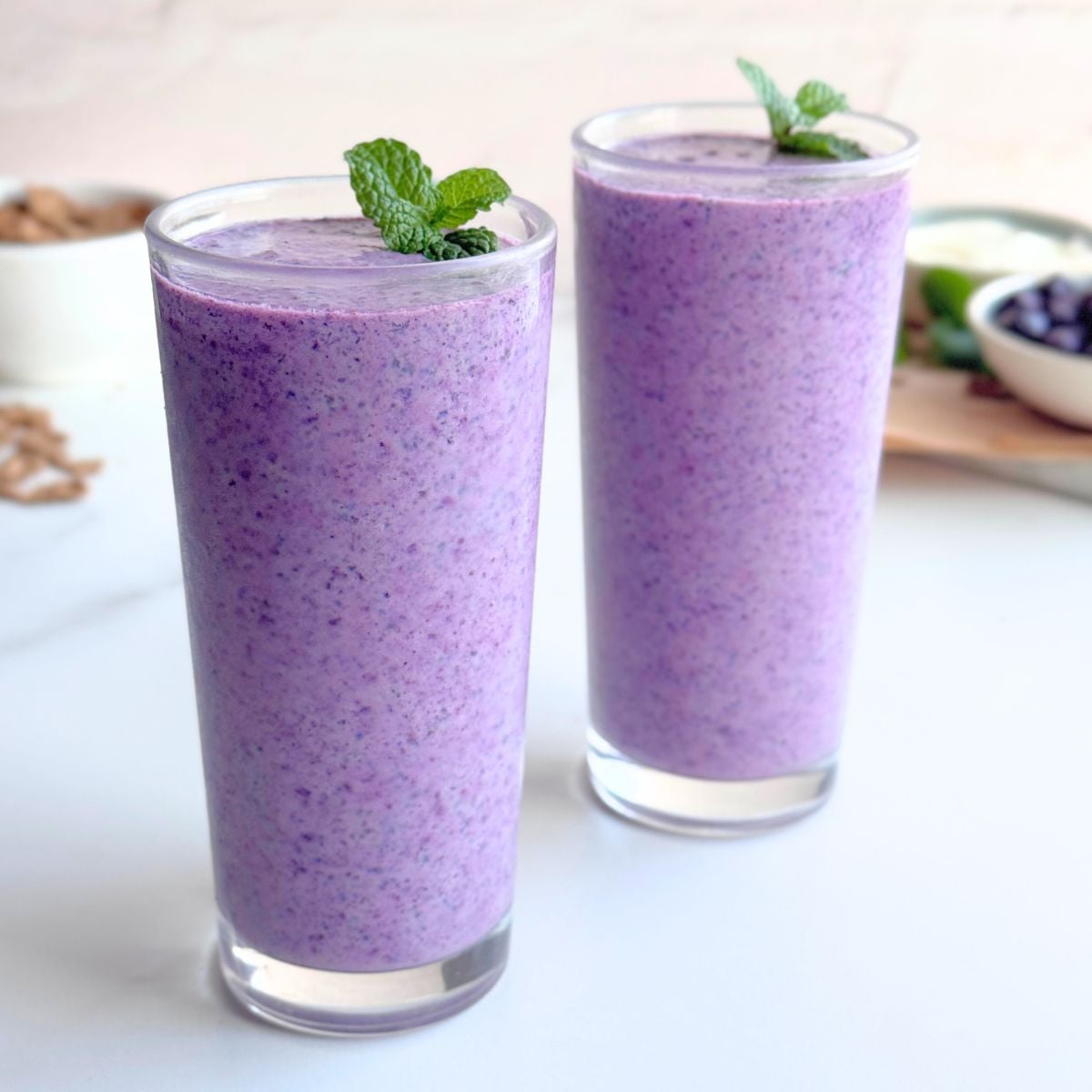 Two glasses of blueberry bran smoothie garnished with fresh mint leaves.