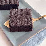 Close-up of a square slice of chocolate sheet cake with rippled buttermilk frosting, served on a gold cake lifter.