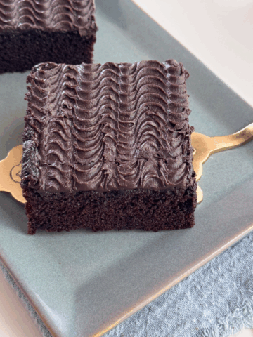 Close-up of a square slice of chocolate sheet cake with rippled buttermilk frosting, served on a gold cake lifter.