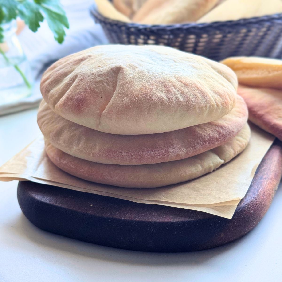 Stack of homemade pita bread with soft puffed pockets on a wooden board lined with parchment paper.