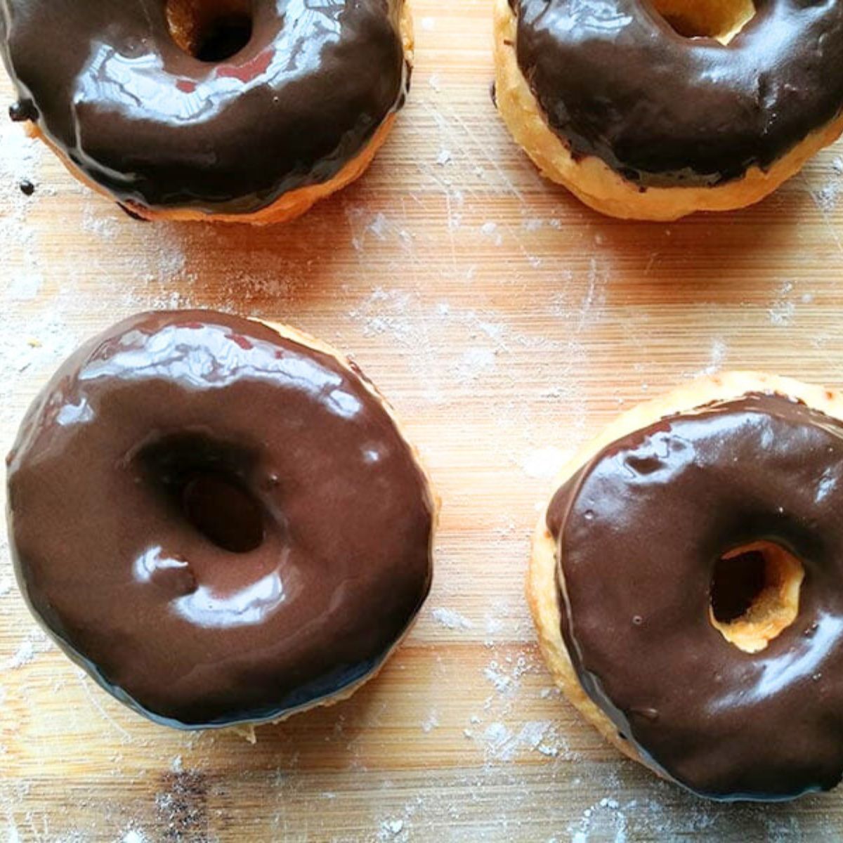 Close-up of 2-ingredient donuts coated in glossy chocolate glaze on a wooden board.