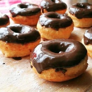 Close-up of golden 2-ingredient donuts coated in glossy chocolate glaze, resting on a floured wooden board