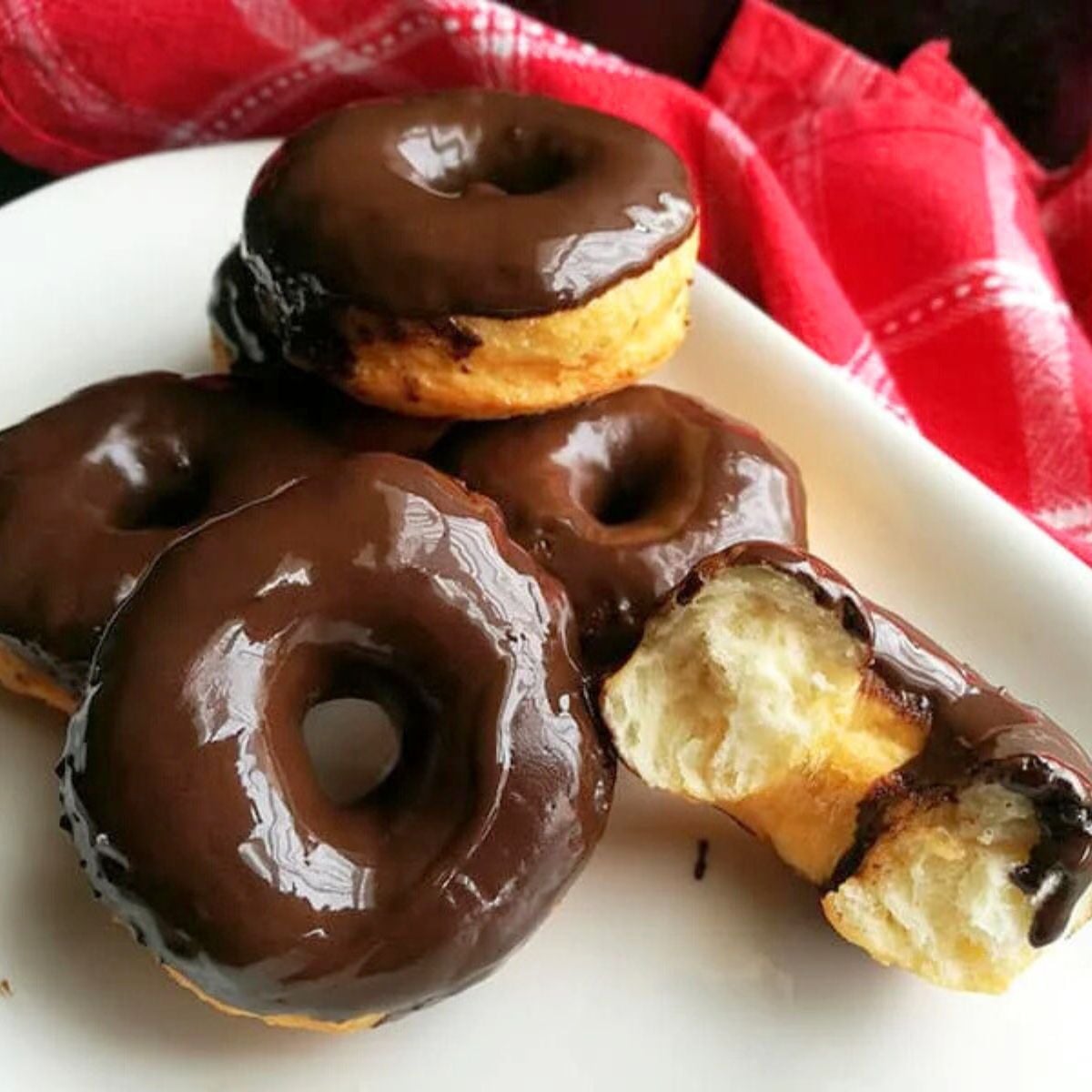 Soft, fluffy donuts topped with chocolate glaze, served on a white plate with a red kitchen cloth