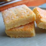 Buttery 3-ingredient shortbread squares stacked on a plate, lightly dusted with sugar.