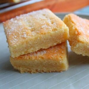 Buttery 3-ingredient shortbread squares stacked on a plate, lightly dusted with sugar.