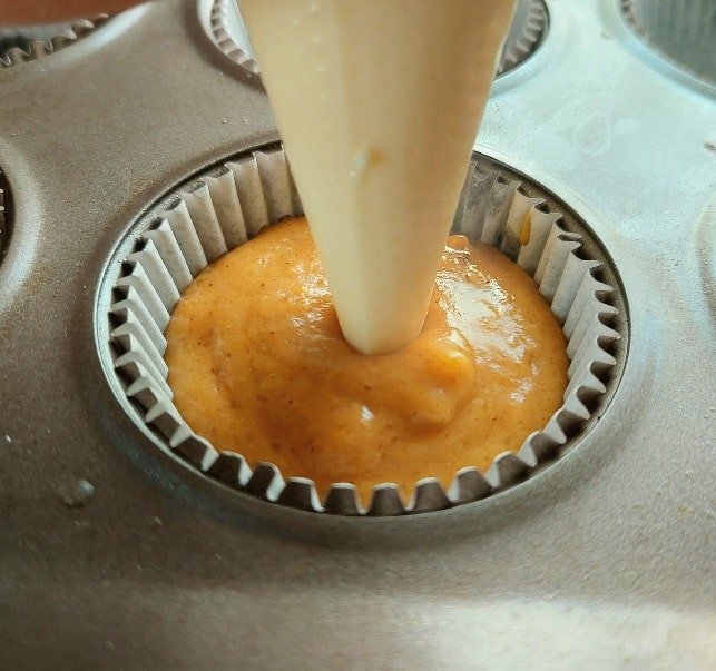 Fill the cream cheese frosting into a piping bag. You can use a piping bag with a tip or just a ziplock bag with the tip cut off. 
Insert it halfway into the batter and pull out, leaving a little dollop at the top. Depending on how much cream cheese you like, you can leave an even bigger dollop on top.