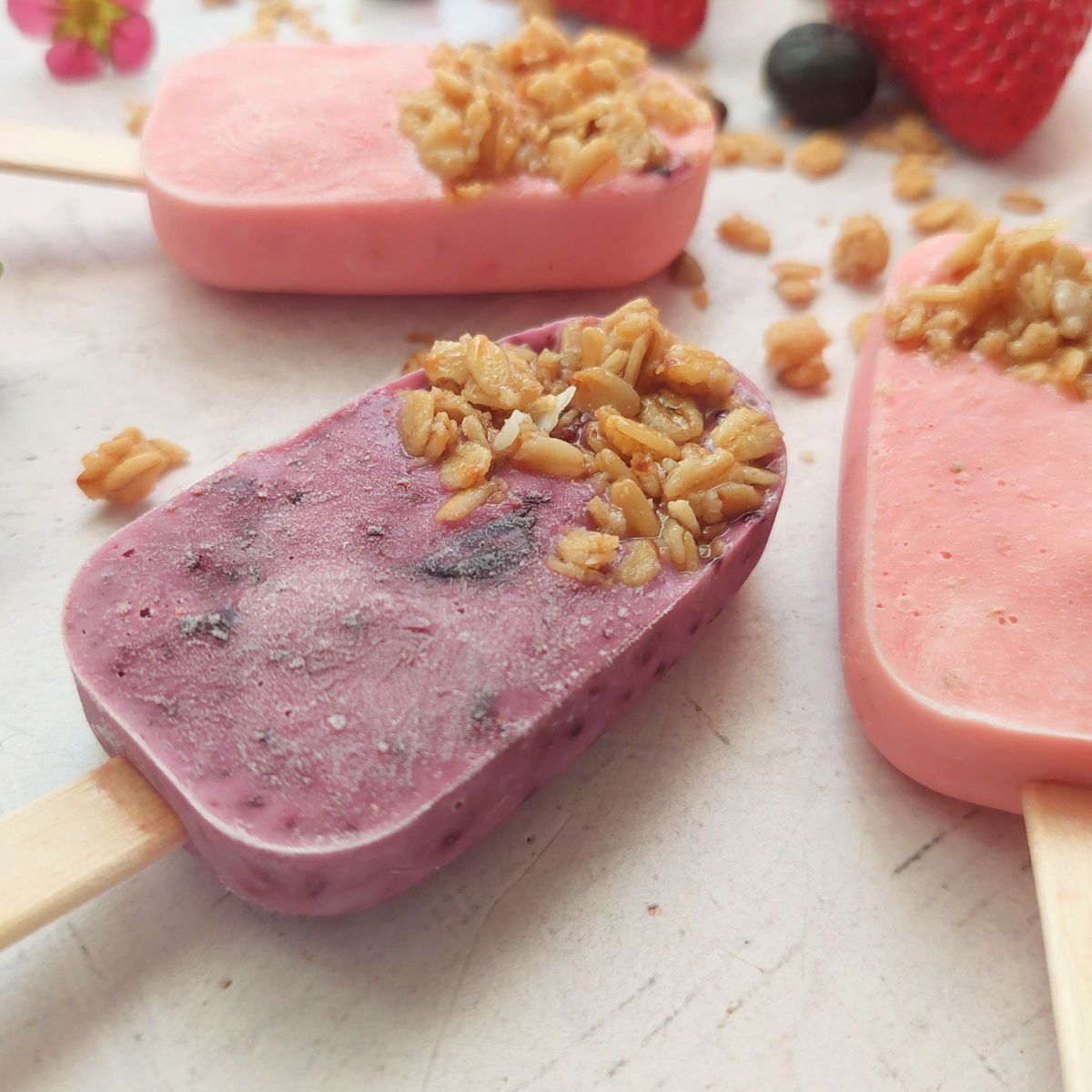 Close-up of homemade blueberry and strawberry yogurt popsicles topped with crunchy granola