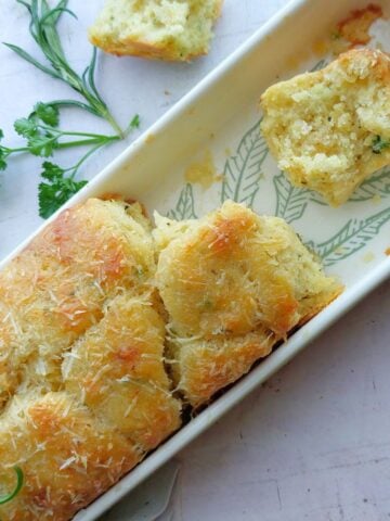 No yeast garlic herb pull-apart bread baked until golden brown in a loaf pan with a piece pulled apart to show the soft interior.