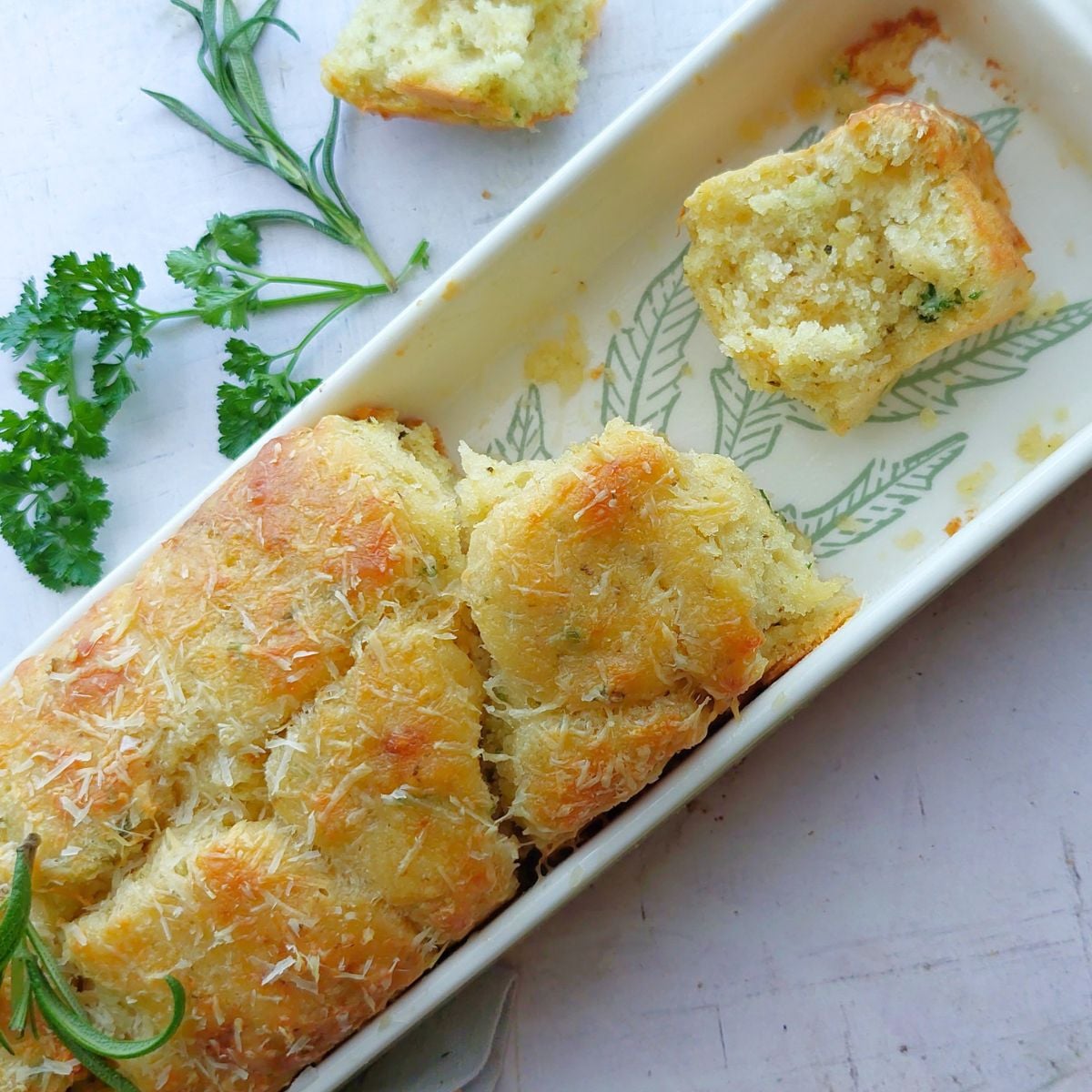 No yeast garlic herb pull-apart bread baked until golden brown in a loaf pan with a piece pulled apart to show the soft interior.