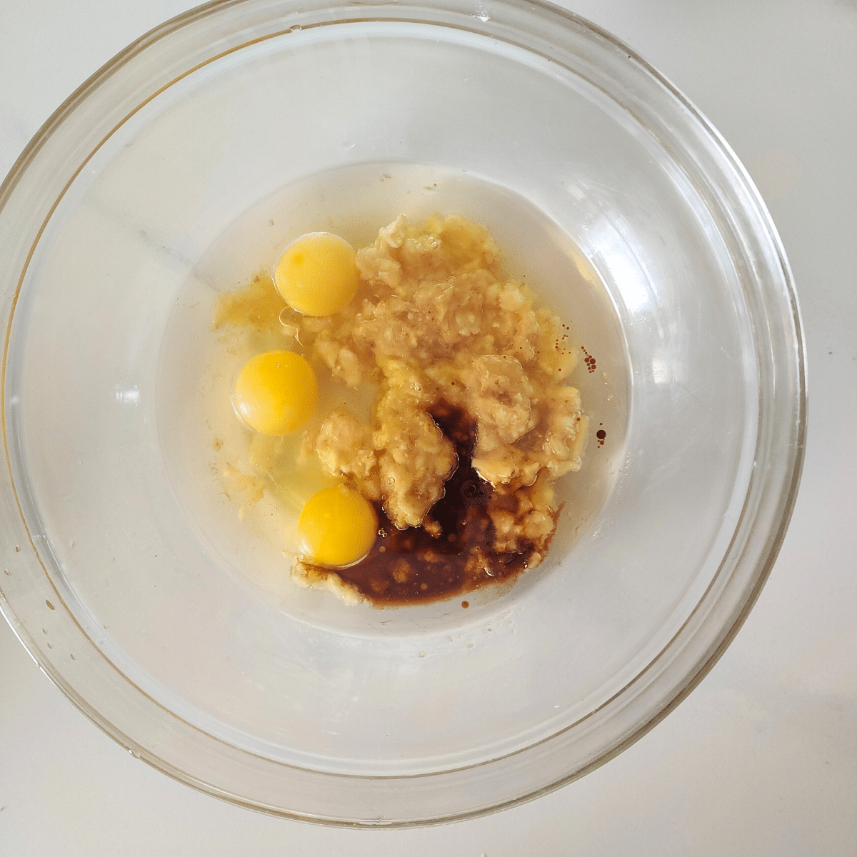 Mashed bananas, oil, eggs, vanilla extract in a bowl