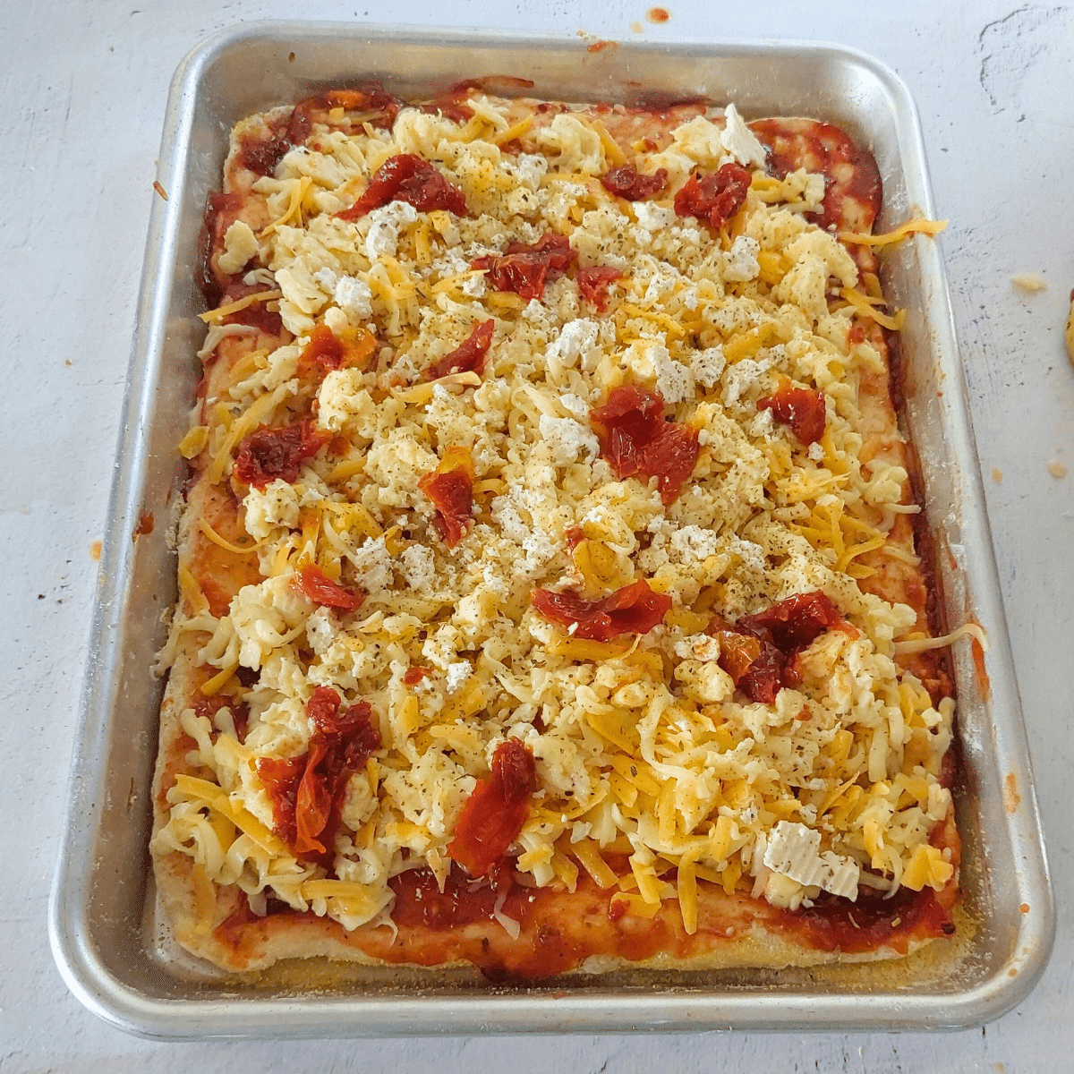  Pre-baked pizza crust topped with tomato relish, shredded cheese, scrambled eggs, feta, and sundried tomatoes, ready to go back in the oven.
