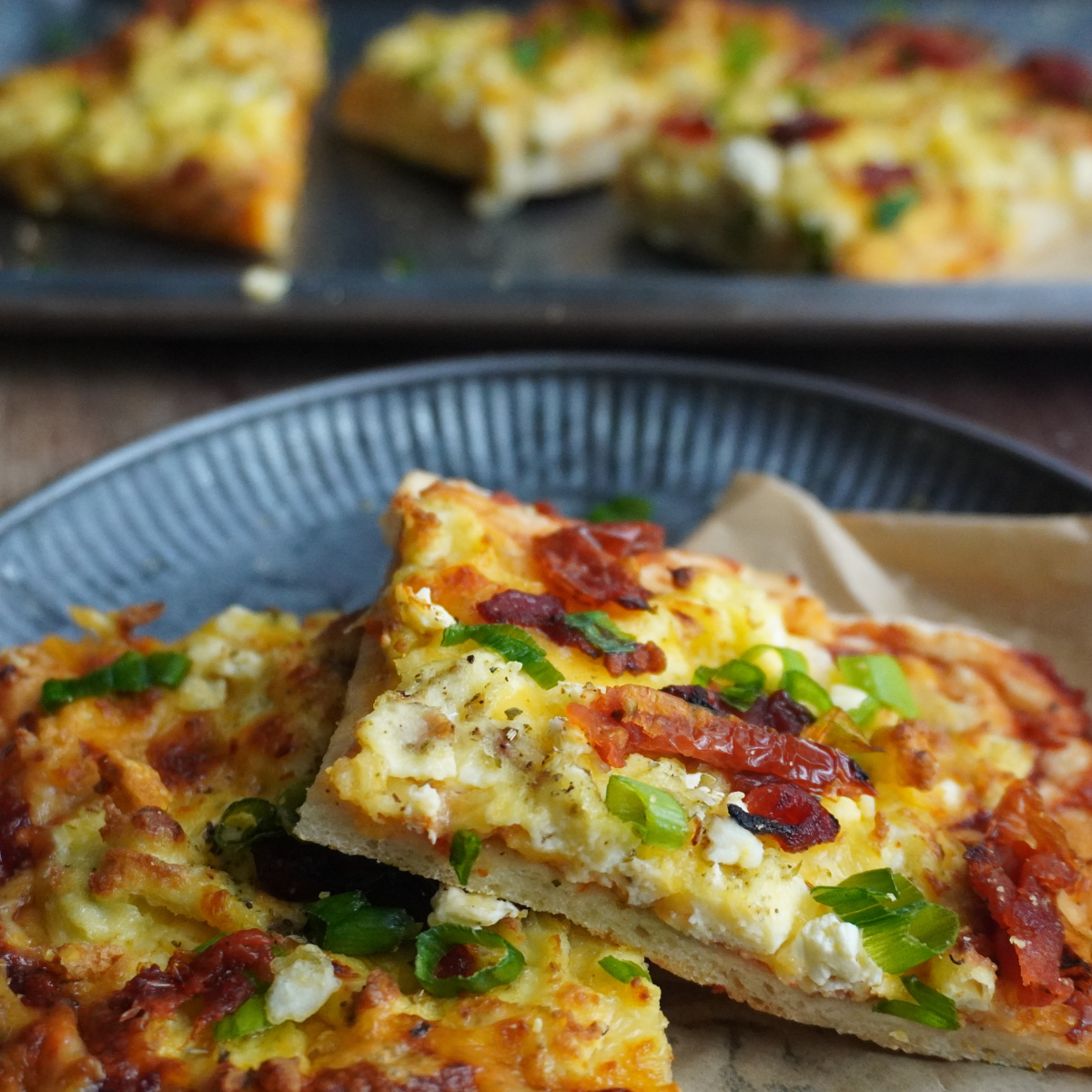 Slices of breakfast pizza topped with scrambled eggs, melted cheddar, sundried tomatoes, and chopped green onions on a soft, golden crust.