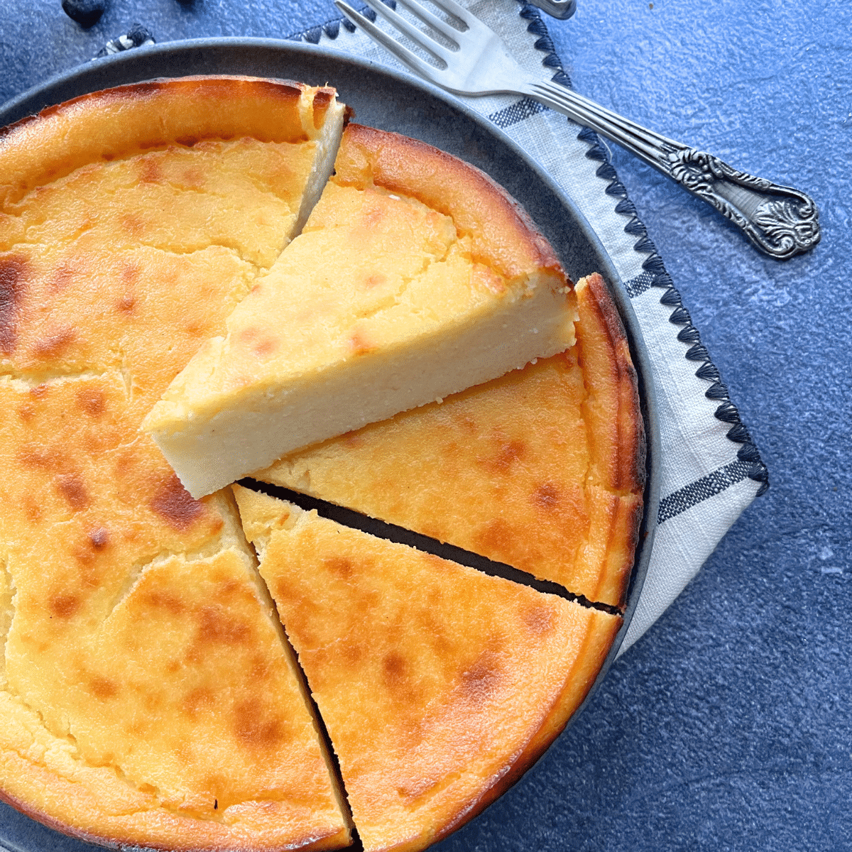 lemon ricotta custard cake with a golden top, sliced and served on a grey plate with a vintage fork and napkin.
