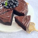 A slice of almond flour chocolate cake with glossy chocolate topping and blueberries on top.