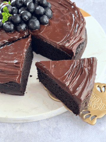 A slice of almond flour chocolate cake with glossy chocolate topping and blueberries on top.