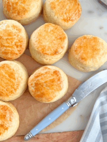 Golden mini cream scones arranged on a marble surface, served with jam and cream in the background.