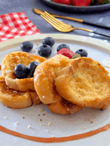 Close-up of mini French toast rounds made with melted ice cream, served with blueberries and strawberries on a white plate.