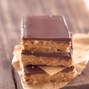 Close-up of chewy chocolate-topped oat bars stacked with parchment paper