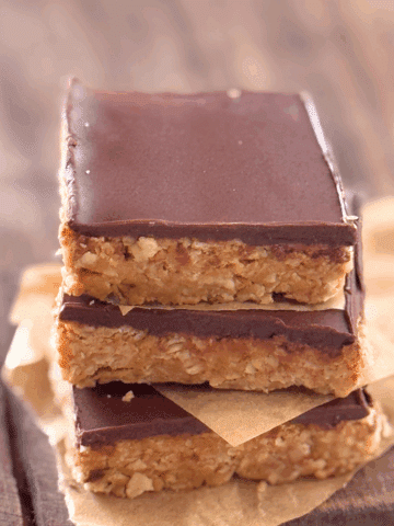 Close-up of chewy chocolate-topped oat bars stacked with parchment paper