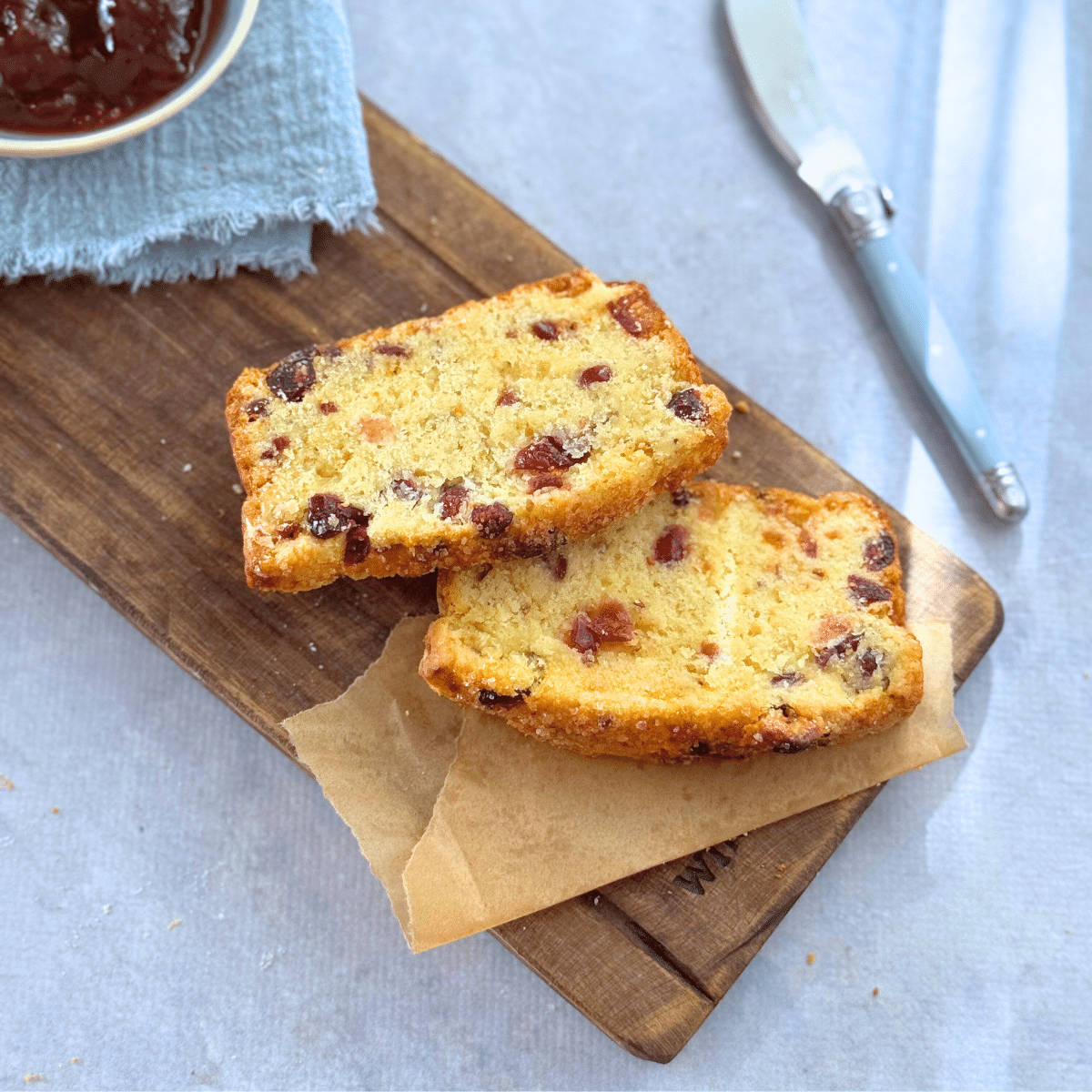 Overhead view of two slices of cranberry cream scone loaf on a wooden board, served with jam