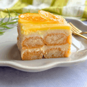 Close-up of a slice of no-bake lemon tiramisu made with ladyfingers, lemon curd, and creamy yogurt, topped with candied lemon slices.