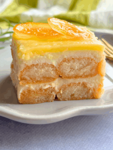 Close-up of a slice of no-bake lemon tiramisu made with ladyfingers, lemon curd, and creamy yogurt, topped with candied lemon slices.