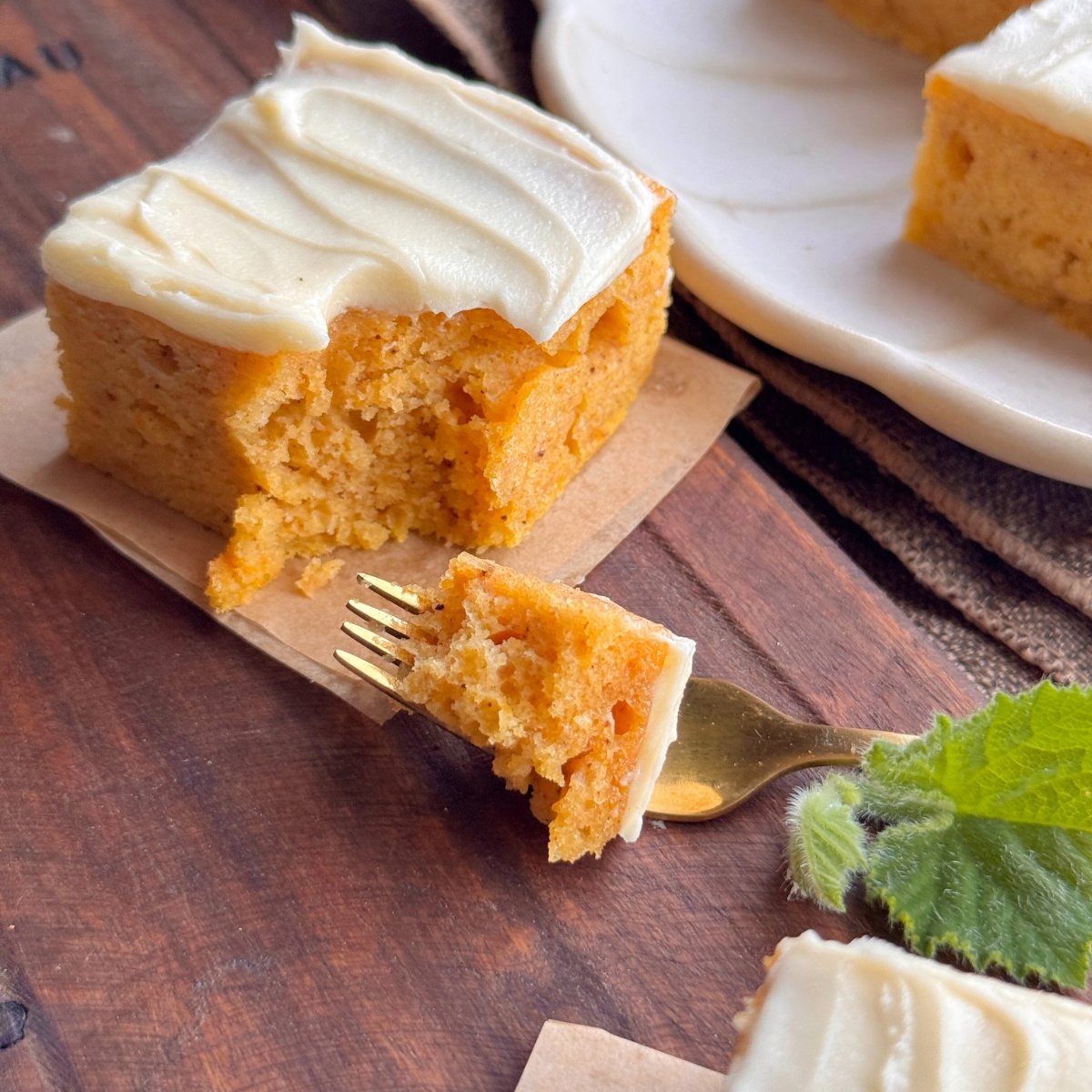 Fork taking a bite from a slice of pumpkin cake with buttercream frosting on a wooden board