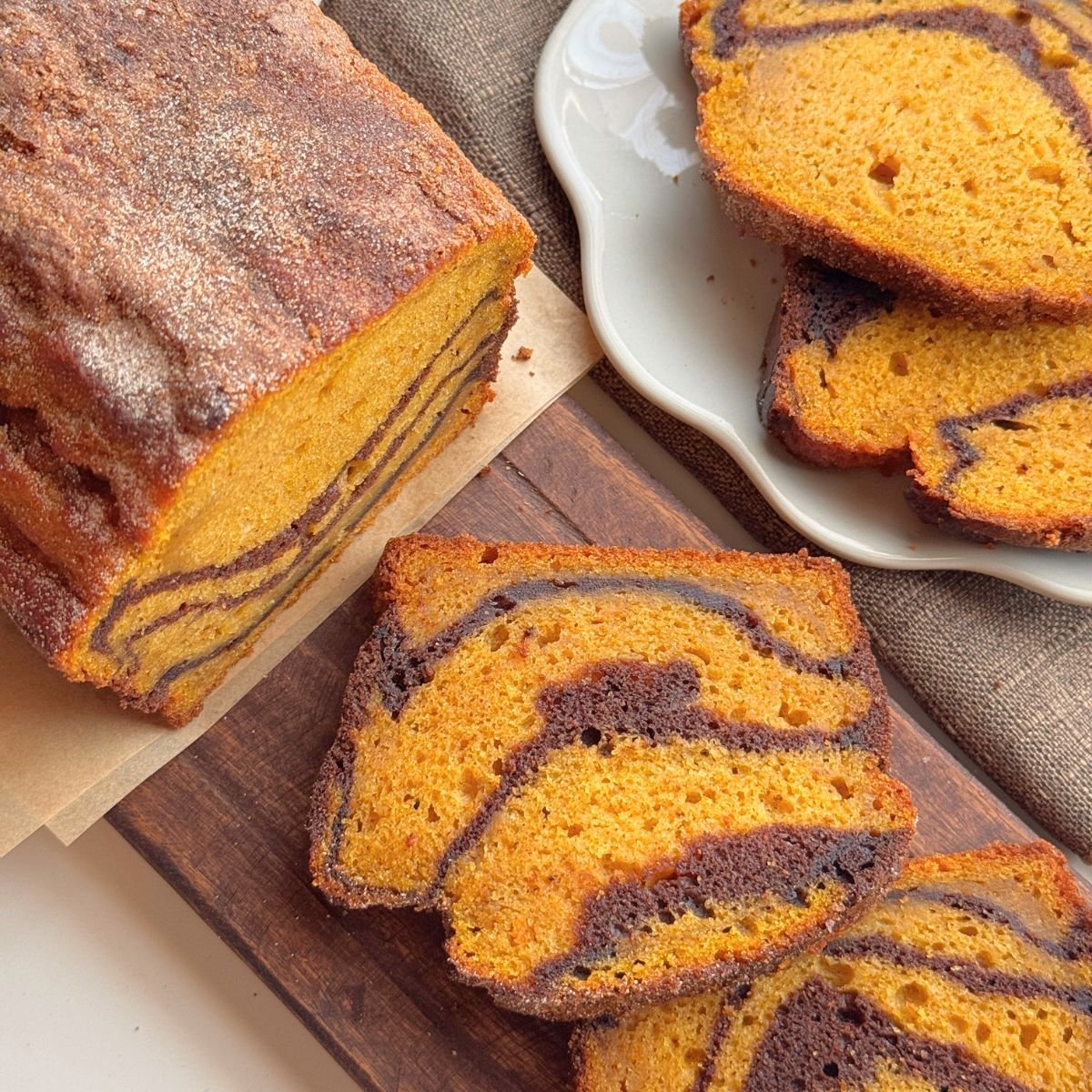 Slices of pumpkin marble cake with chocolate swirls on a wooden board and plate.