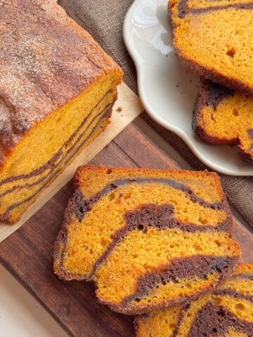 Slices of pumpkin marble cake with chocolate swirls on a wooden board and plate.