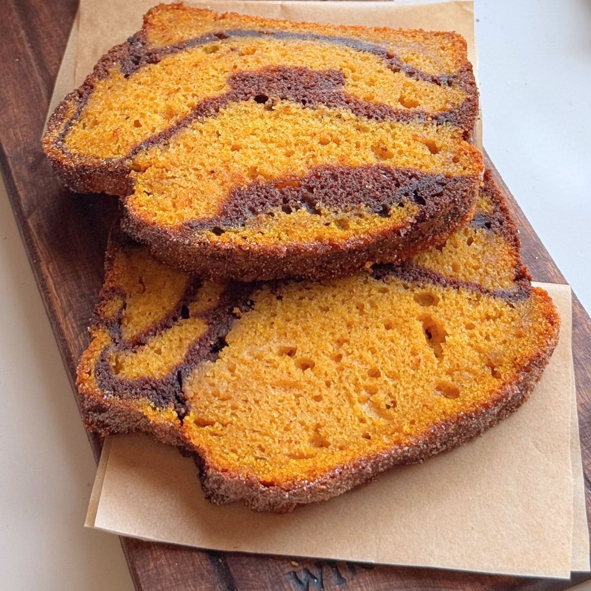 Slices of pumpkin marble cake with chocolate swirls stacked on parchment paper.