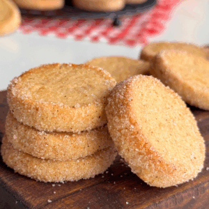 Crisp pumpkin butter cookies stacked on a wooden board, coated in sugar and baked until golden.