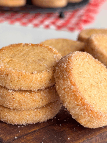 Crisp pumpkin butter cookies stacked on a wooden board, coated in sugar and baked until golden.
