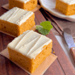 Pumpkin cake topped with creamy buttercream frosting, sliced neatly on a wooden board — simple comfort and classic homemade style.