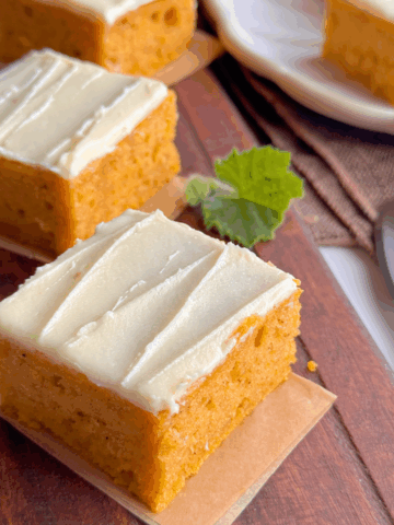 Pumpkin cake topped with creamy buttercream frosting, sliced neatly on a wooden board — simple comfort and classic homemade style.