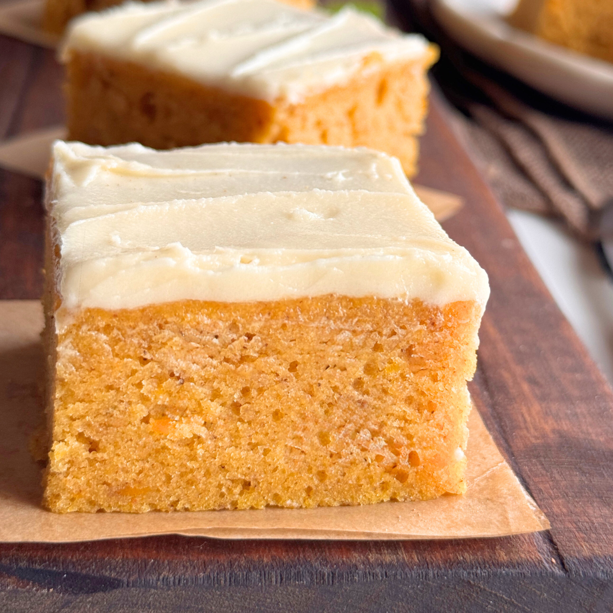 Close-up of a slice of pumpkin cake with buttercream frosting, showing a soft, even texture and smooth creamy top on a wooden board.