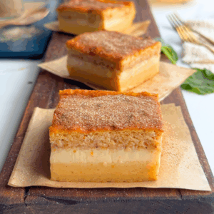 Pumpkin custard cake sliced to show 3 layers and served on parchment placed on board
