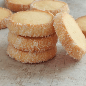 Stacked French butter cookies rolled in sugar on a light rustic board.