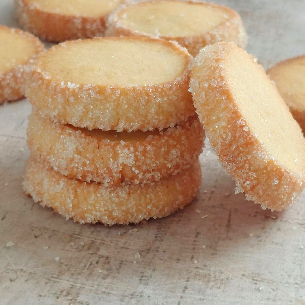 Stacked French butter cookies rolled in sugar on a light rustic board.