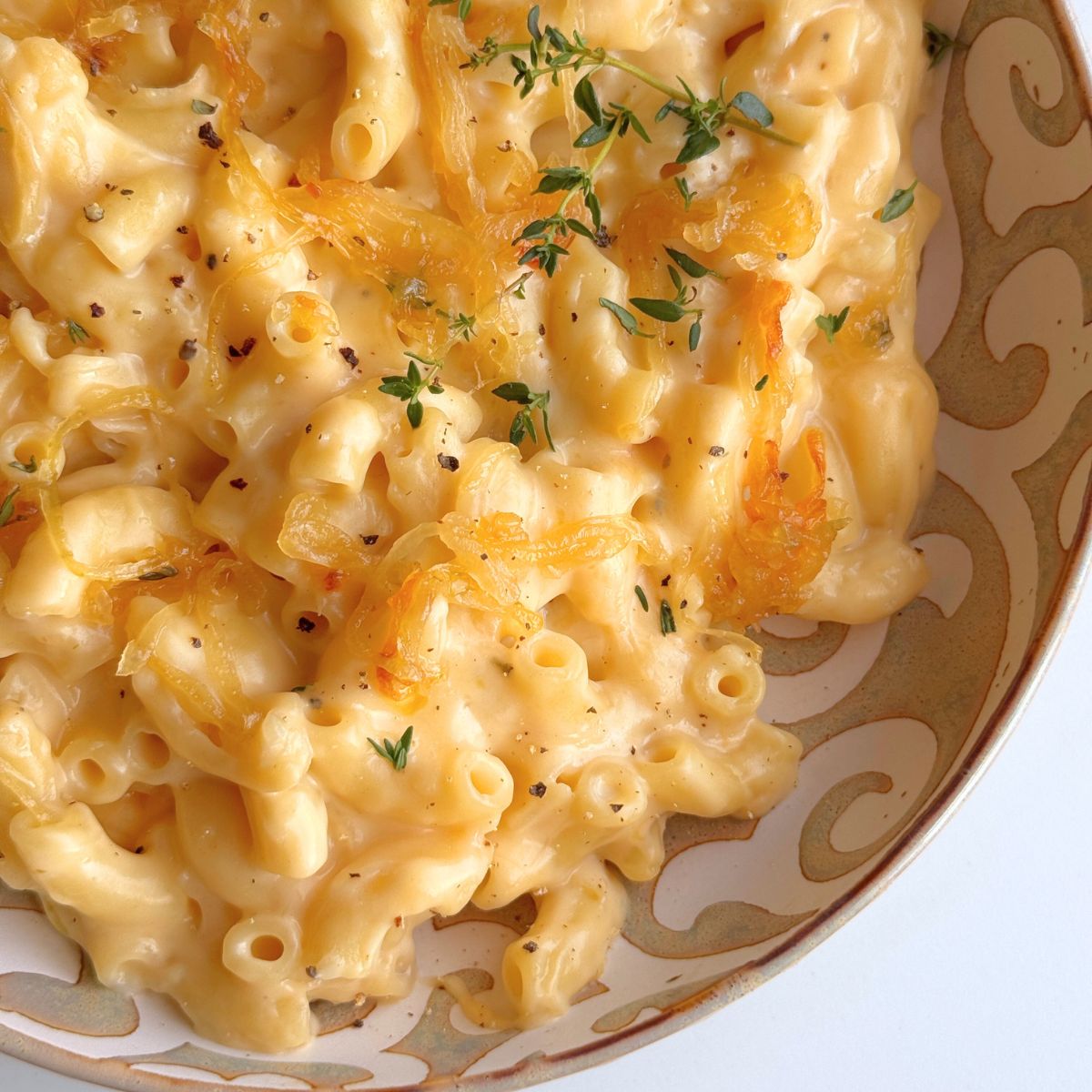 Close-up of creamy French onion mac and cheese showing golden caramelized onions and thyme.