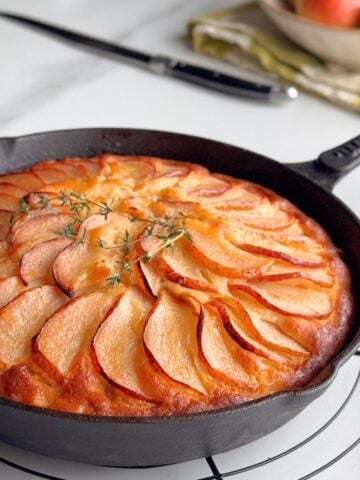 Golden pear cake baked in a cast-iron skillet, topped with caramelized pear slices and fresh thyme.