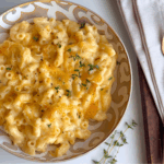 Bowl of creamy French onion mac and cheese topped with caramelized onions and thyme, on a neutral napkin.