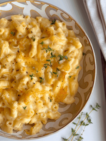 Bowl of creamy French onion mac and cheese topped with caramelized onions and thyme, on a neutral napkin.