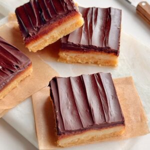 No-bake millionaire’s shortbread bars with defined chocolate, caramel, and shortbread layers arranged on parchment paper
