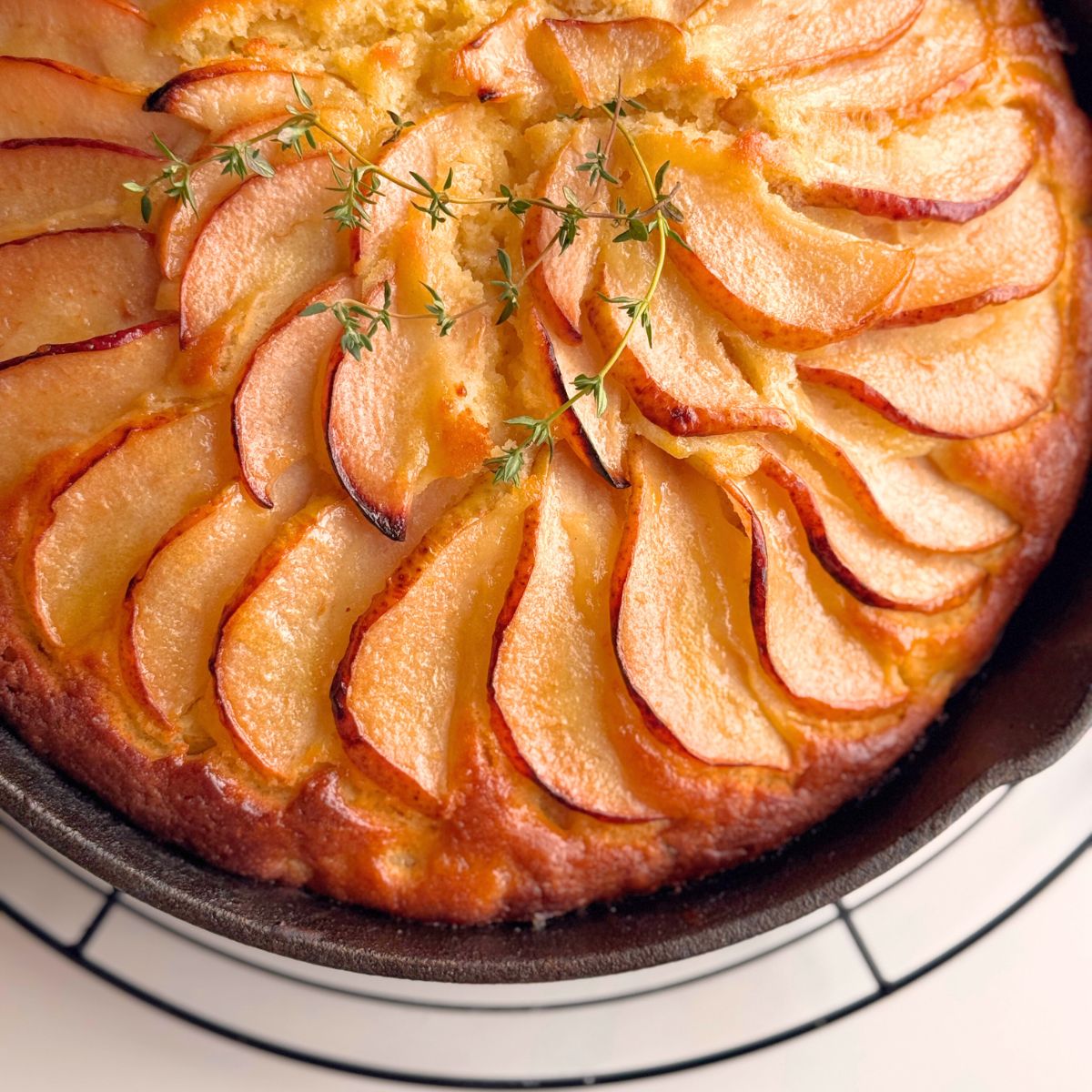 Close-up of a pear cake slice with red-blush pear topping and sprig of thyme