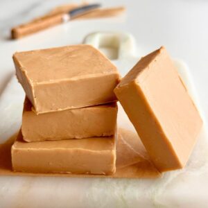Stacked pieces of smooth 2-ingredient Biscoff fudge made with white chocolate on a marble board.
