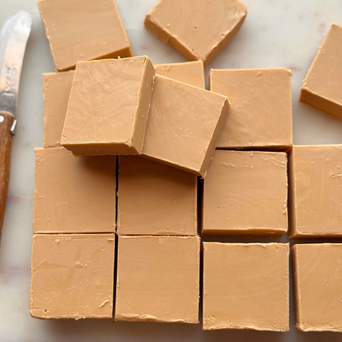 Squares of chilled Biscoff fudge cut into neat blocks on a marble board, showing smooth, creamy texture.