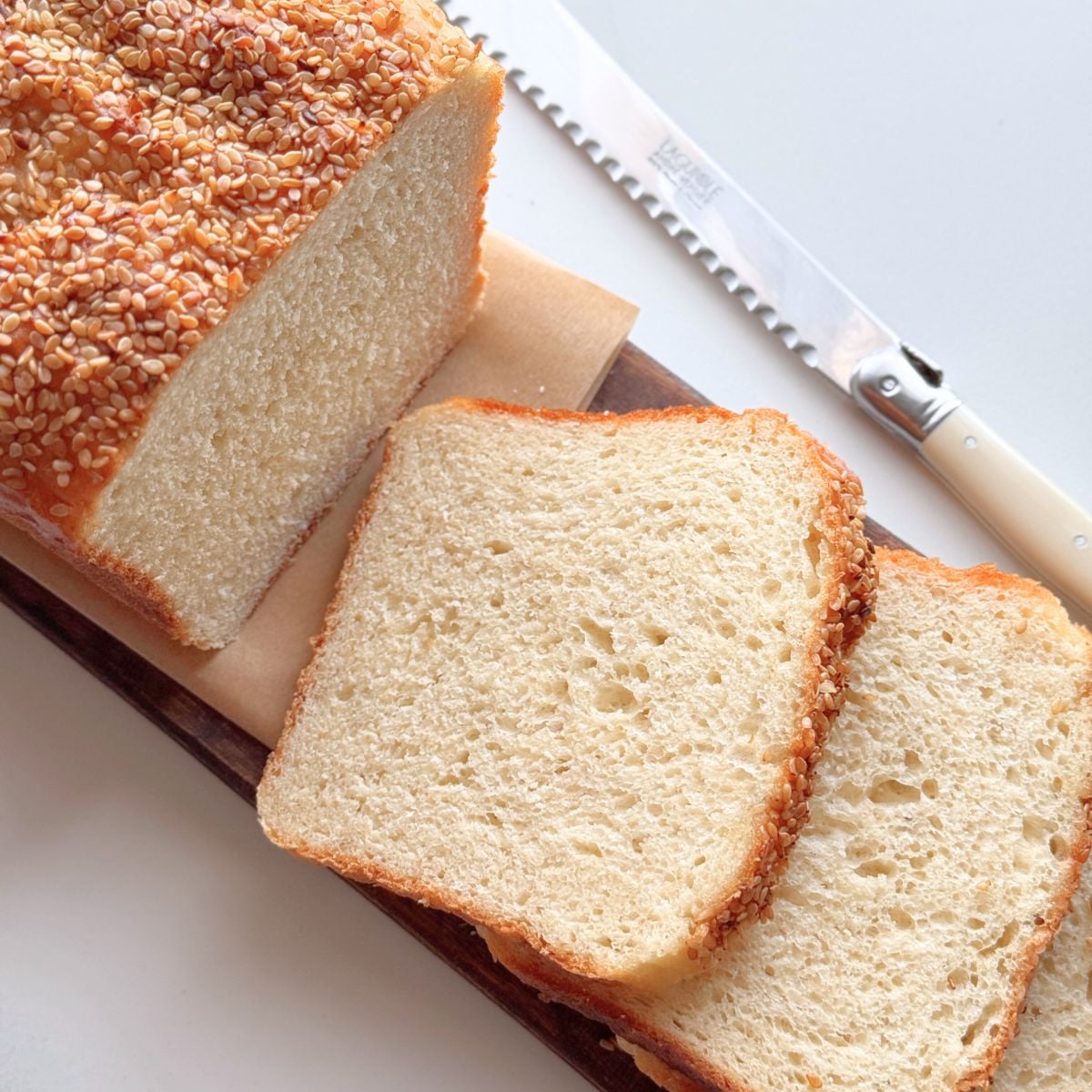 No knead buttermilk bread loaf with sesame seed topping, sliced to show a soft homemade crumb.